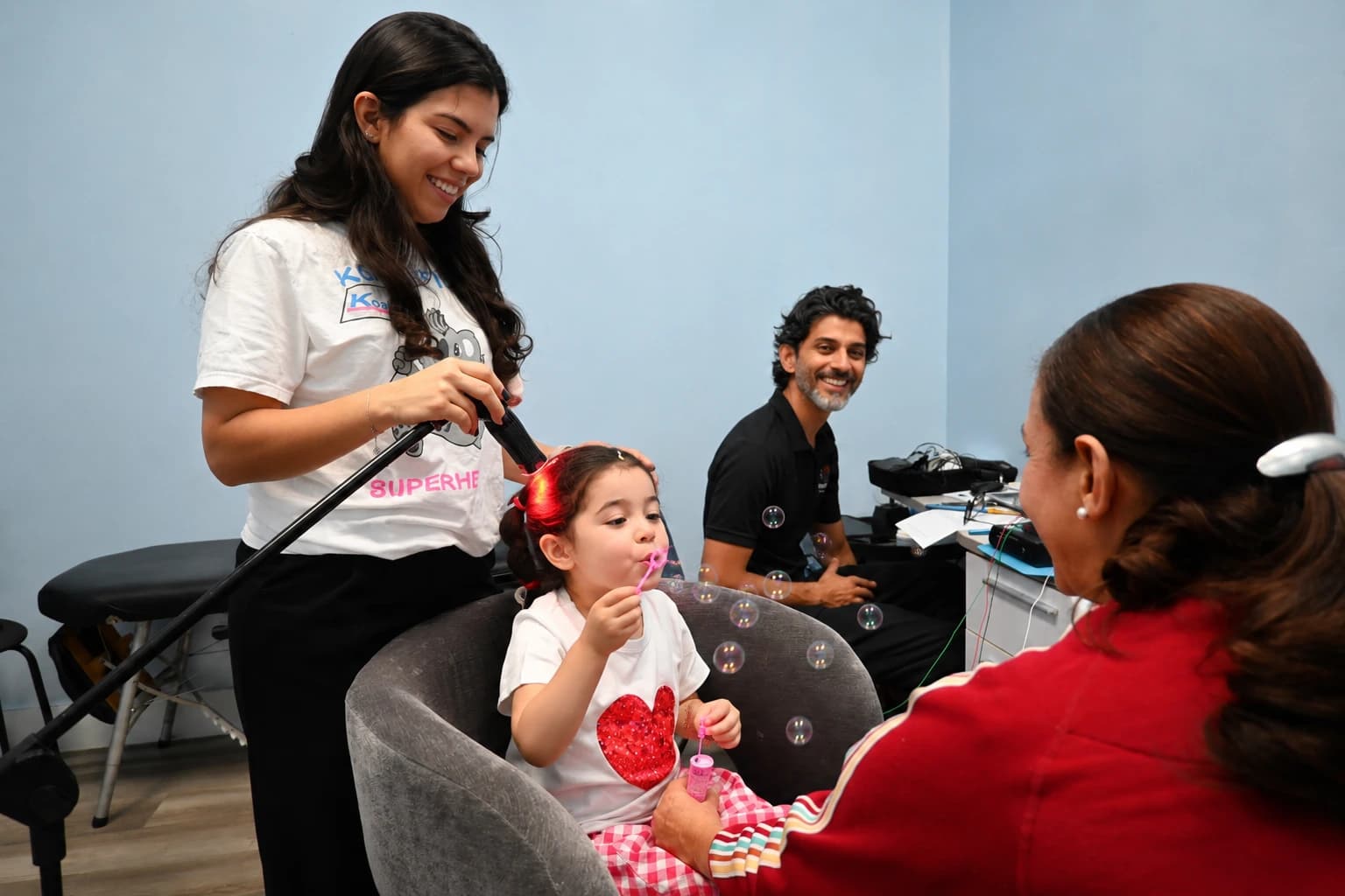 A therapist holding a device near a young girl’s temple while a parent watches
