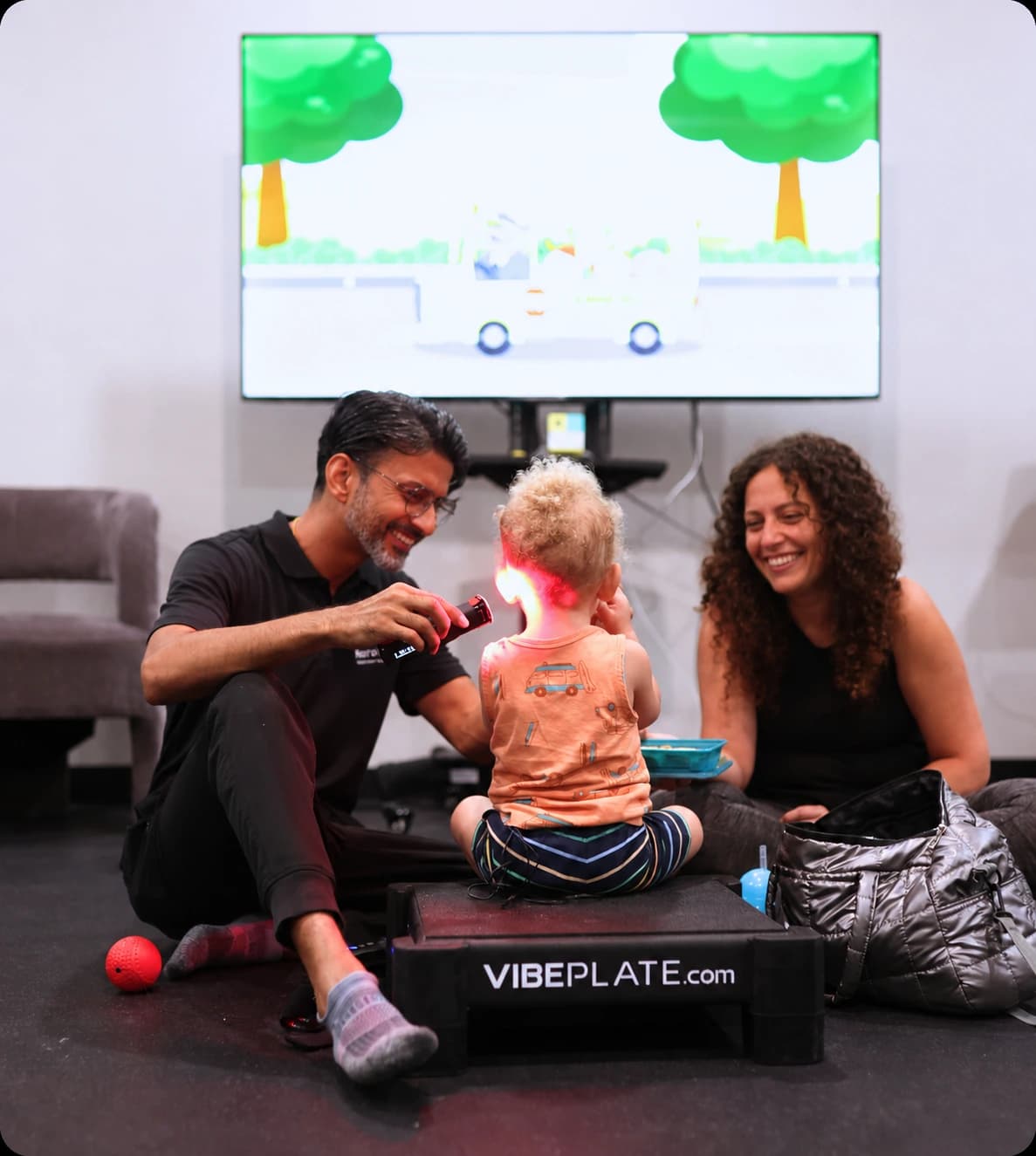 A therapist and a mother working with a toddler using a red therapy light