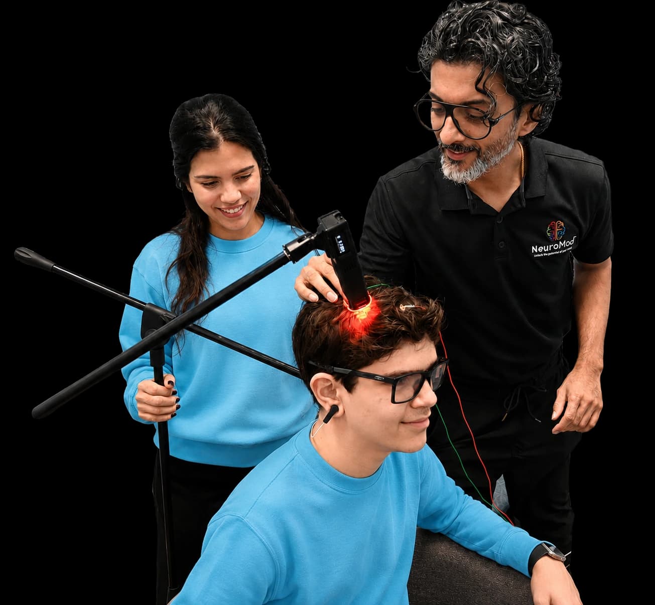 A NeuroMod clinician guiding a laser device over a seated boy while an assistant steadies it